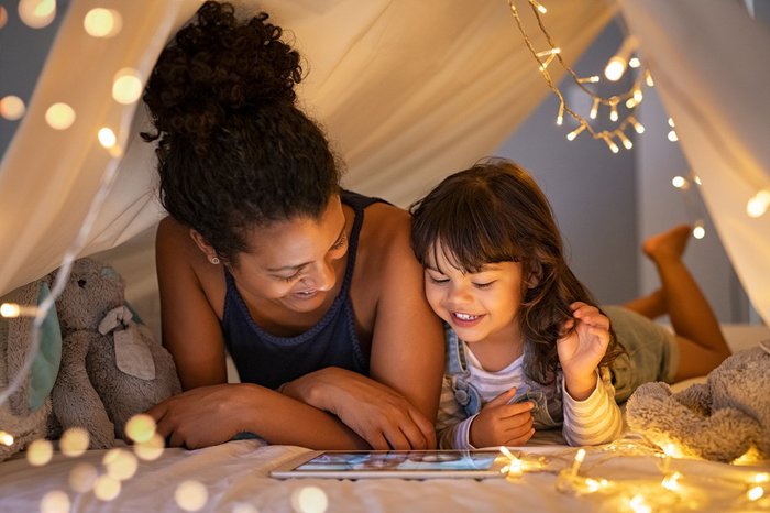 Mother and daughter smiling and using tablet in a child's indoor tent