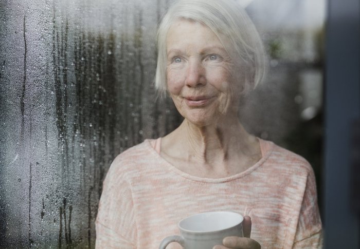 Older woman smiling behind wet window