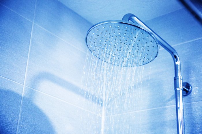 Shower head switched on in a blue tiled bathroom