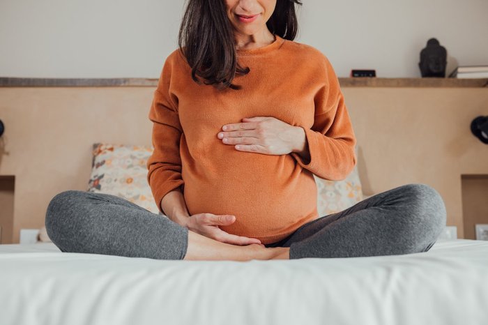 Smiling pregnant woman sat on a bed and holding her bump